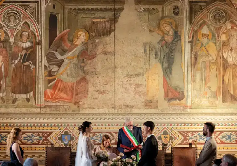 Civil wedding ceremony before Renaissance frescoes, officiant wearing the Italian tricolour sash